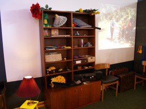 En rigtig pulterkammerreol fyldt med kunstige blomster, legetøjsbiler, en båndoptager og alt muligt andet. I baggrunden ses et af vores fine originale 70'er lysbilleder.